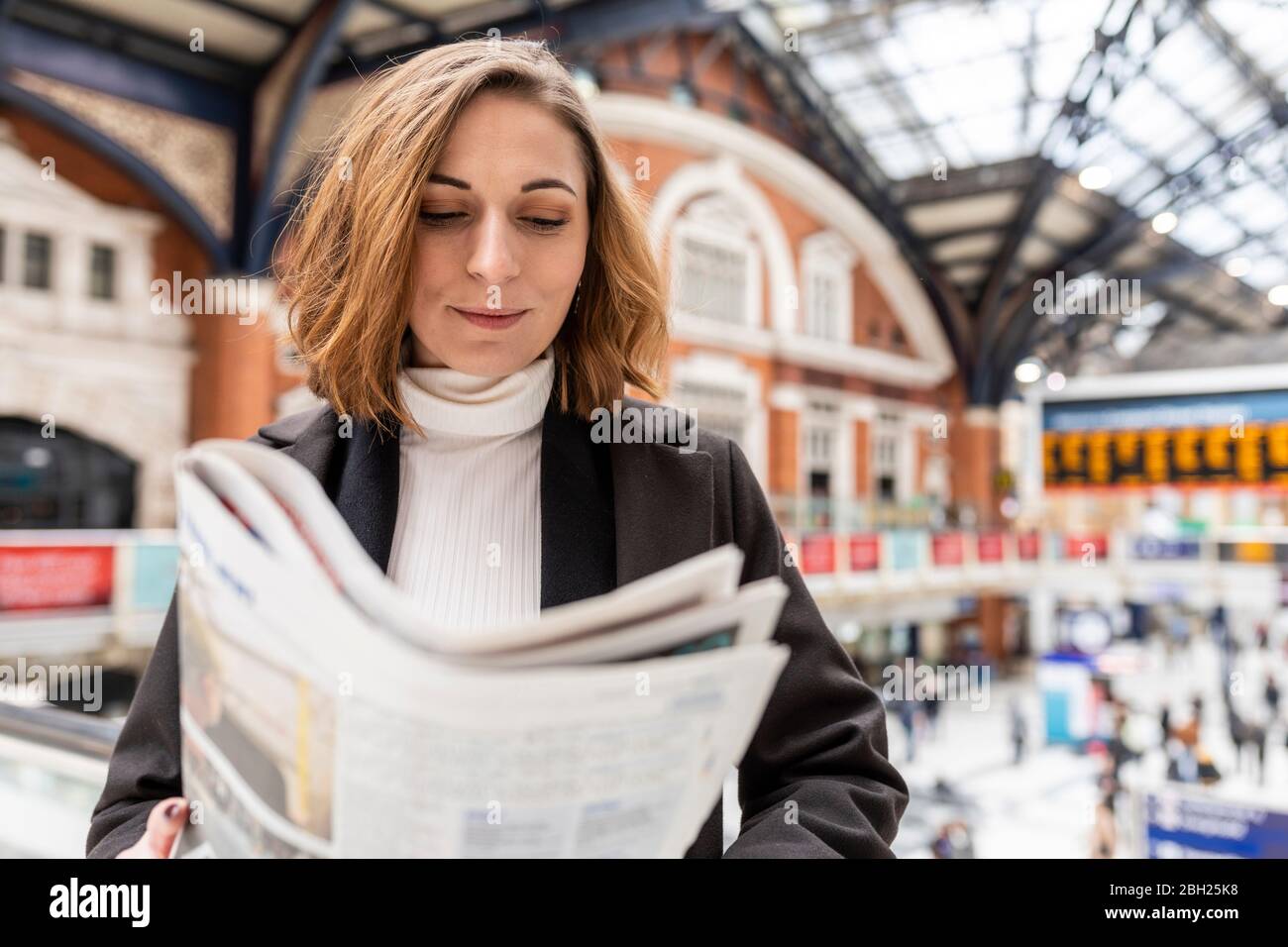 Woman at train station reading a newspaper, London, UK Stock Photo