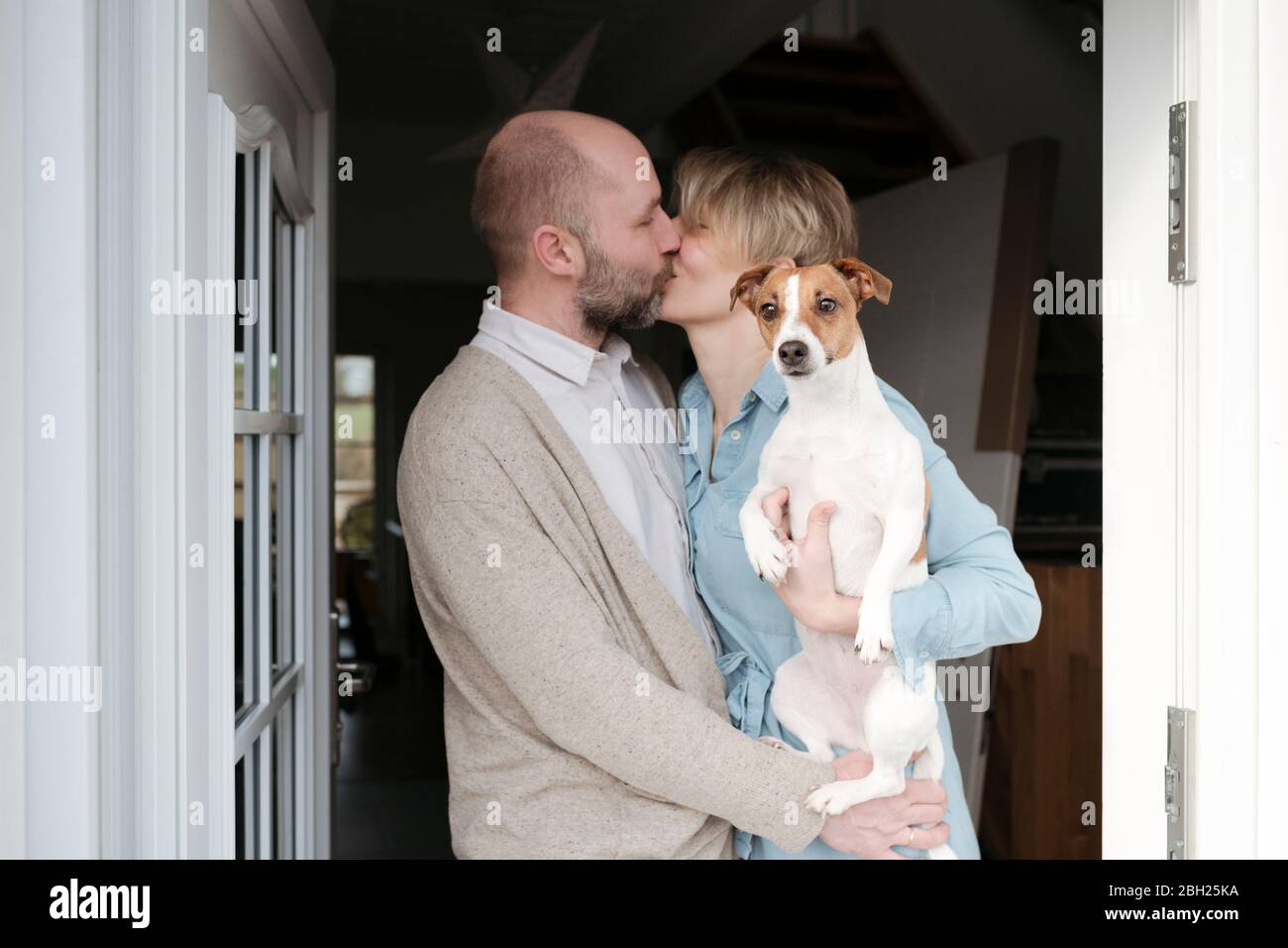 Happy couple with dog kissing at the entrance of their house Stock Photo