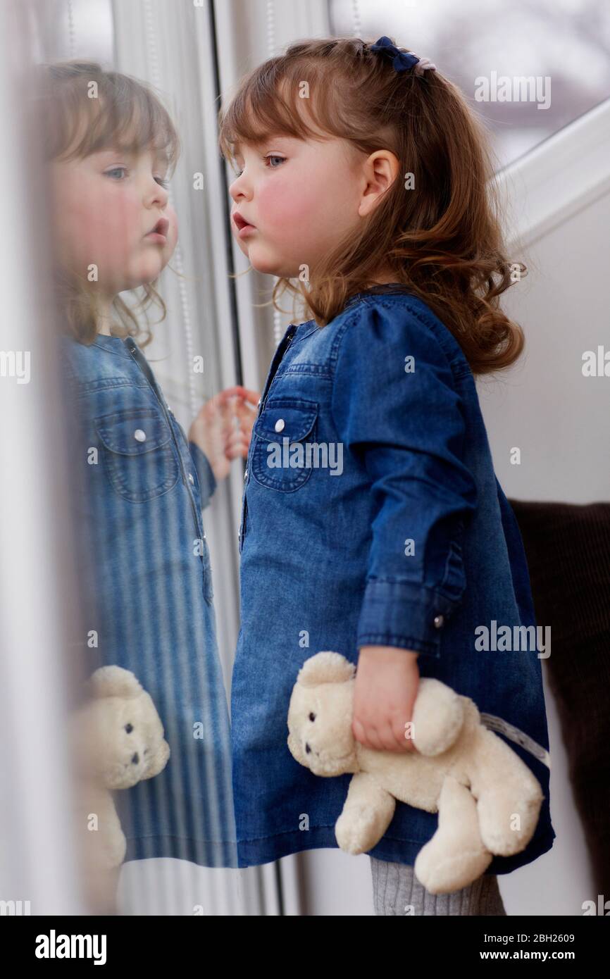 Portrait of curios toddler girl with teddy bear watching something Stock Photo