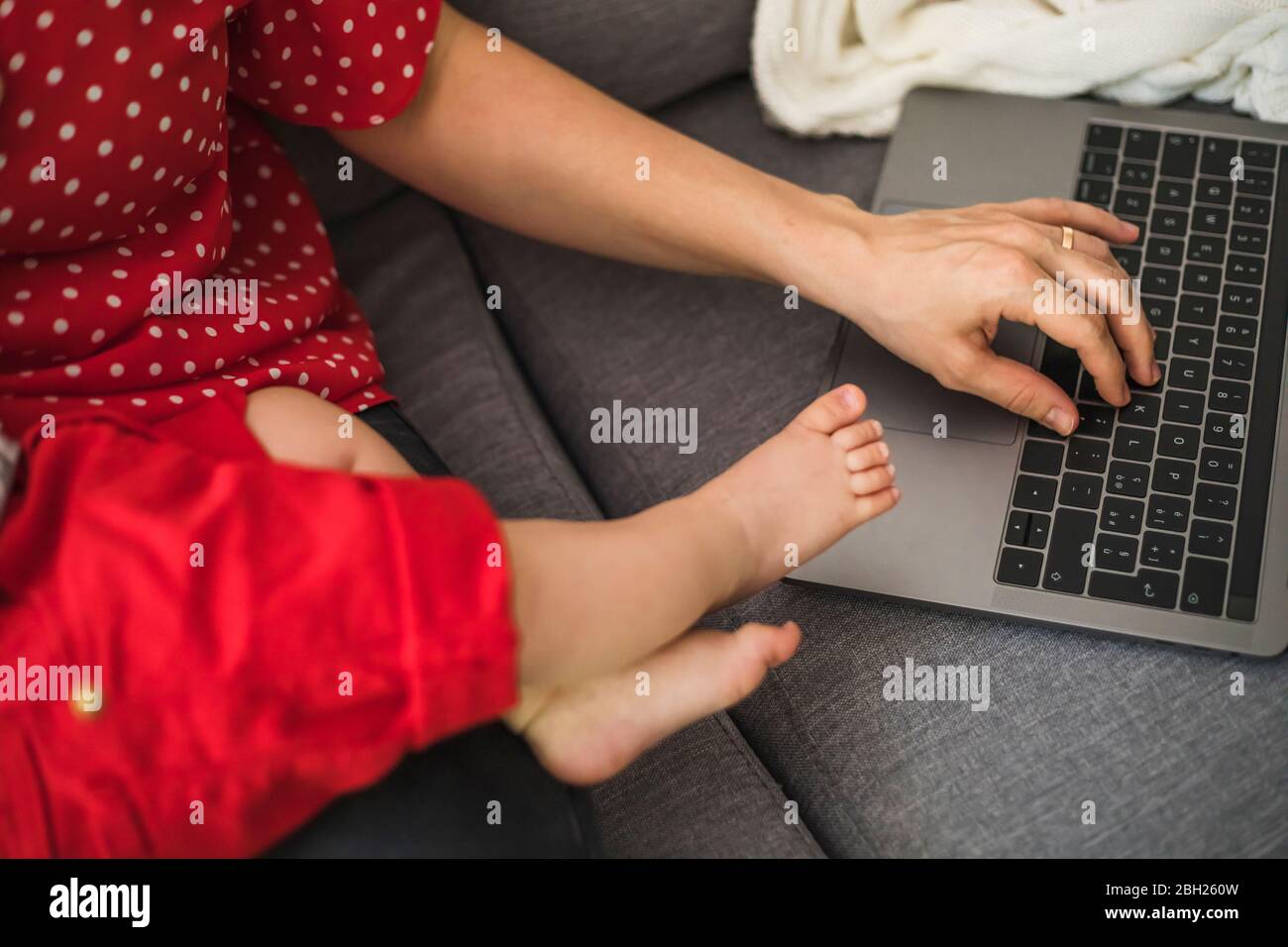 Mother remote working with laptop on sofa while holding her sleepy baby boy Stock Photo