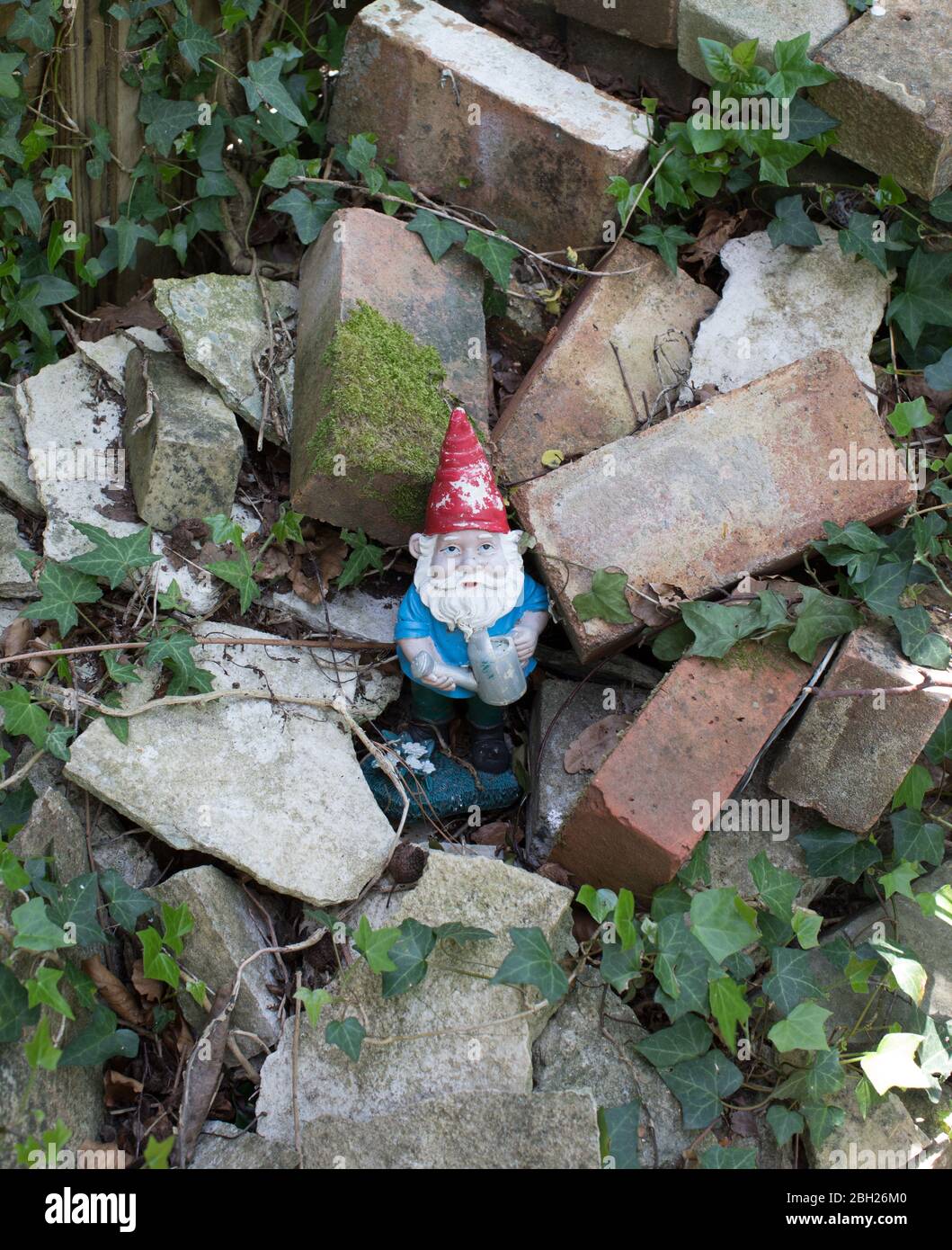 An old garden gnome standing in a pile of used bricks Stock Photo