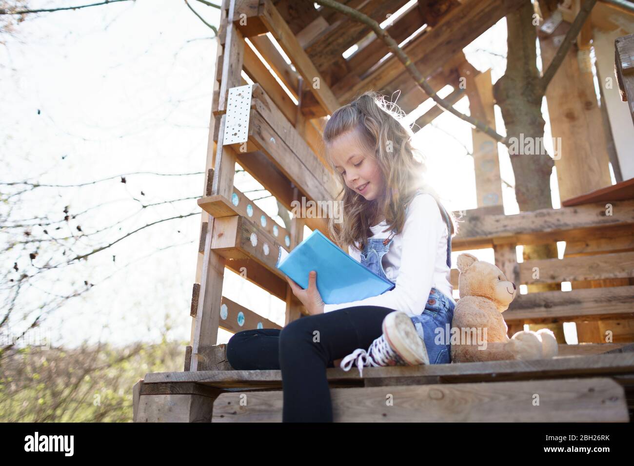 Girl sitting in garden at tree house and writing something in her blue diary Stock Photo