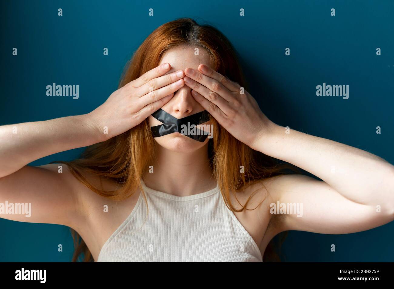 Portrait of young woman with taped mouth covering her eyes Stock Photo