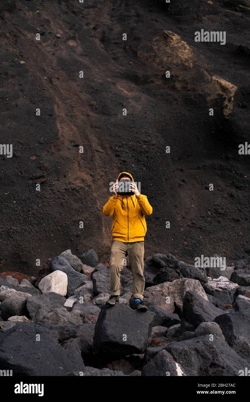 Man standing amidst volcanic rocks covering his face, Sao Miguel Island, Azores, Portugal Stock Photo