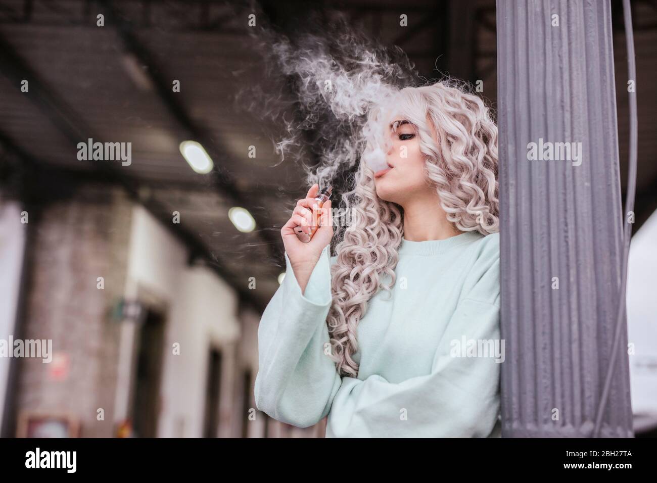 Young woman smoking electronic cigarette on platform Stock Photo