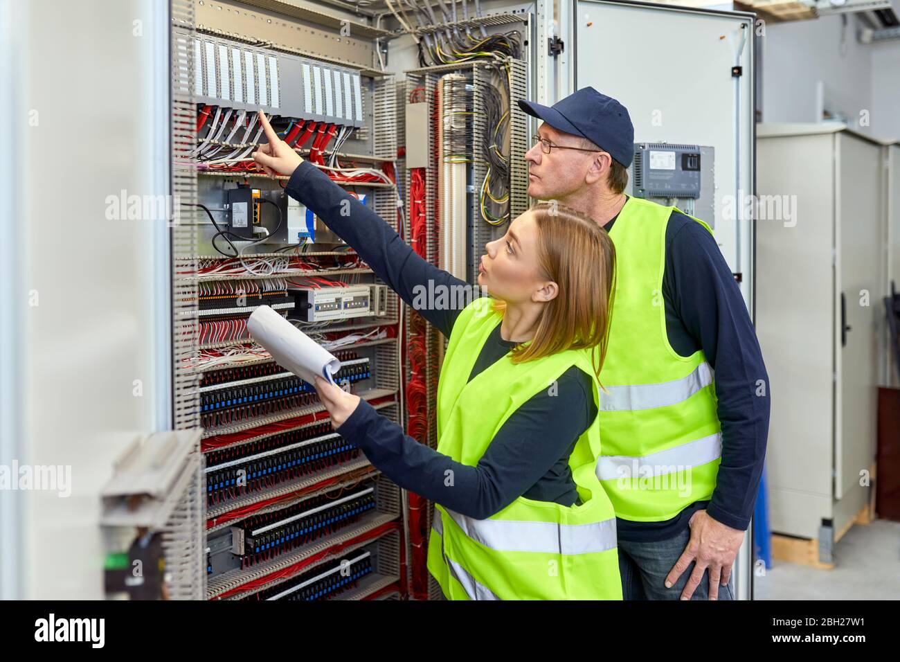 Two electricians with plan looking at fuse box Stock Photo
