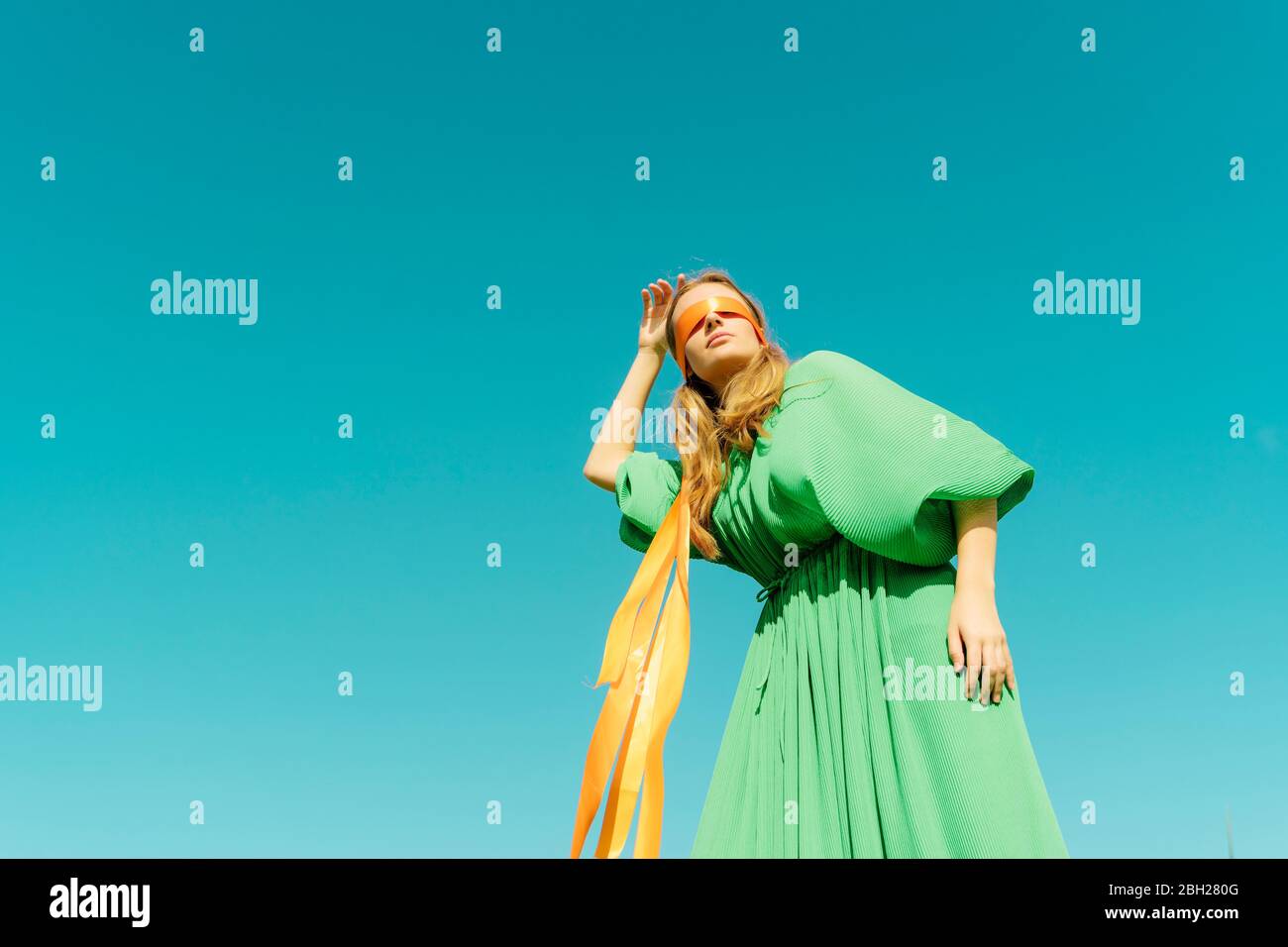 Blindfolded young woman wearing a green dress under blue sky Stock Photo