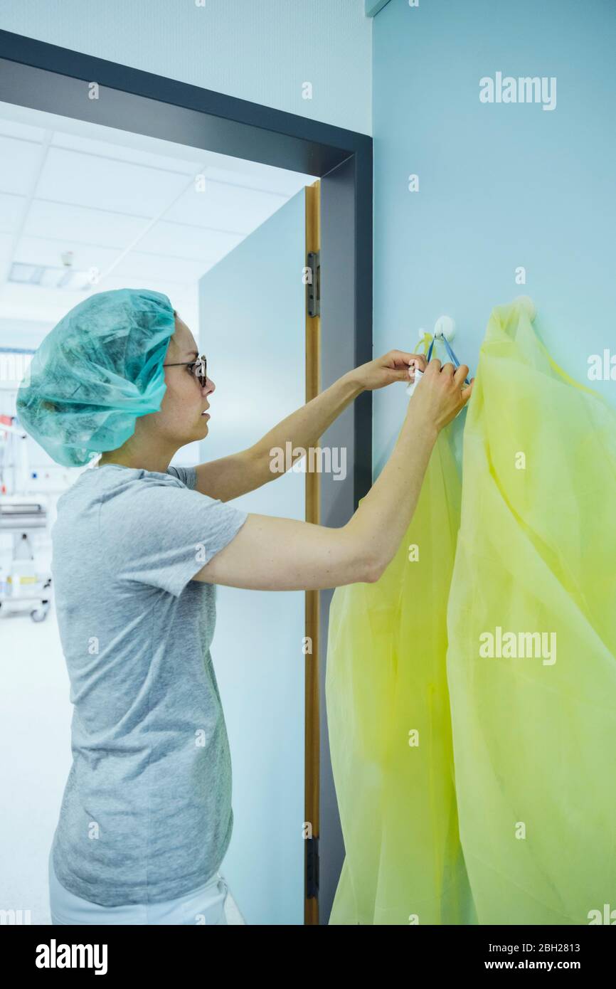 Doctor taking personal protective equipment from hook in hospital Stock Photo