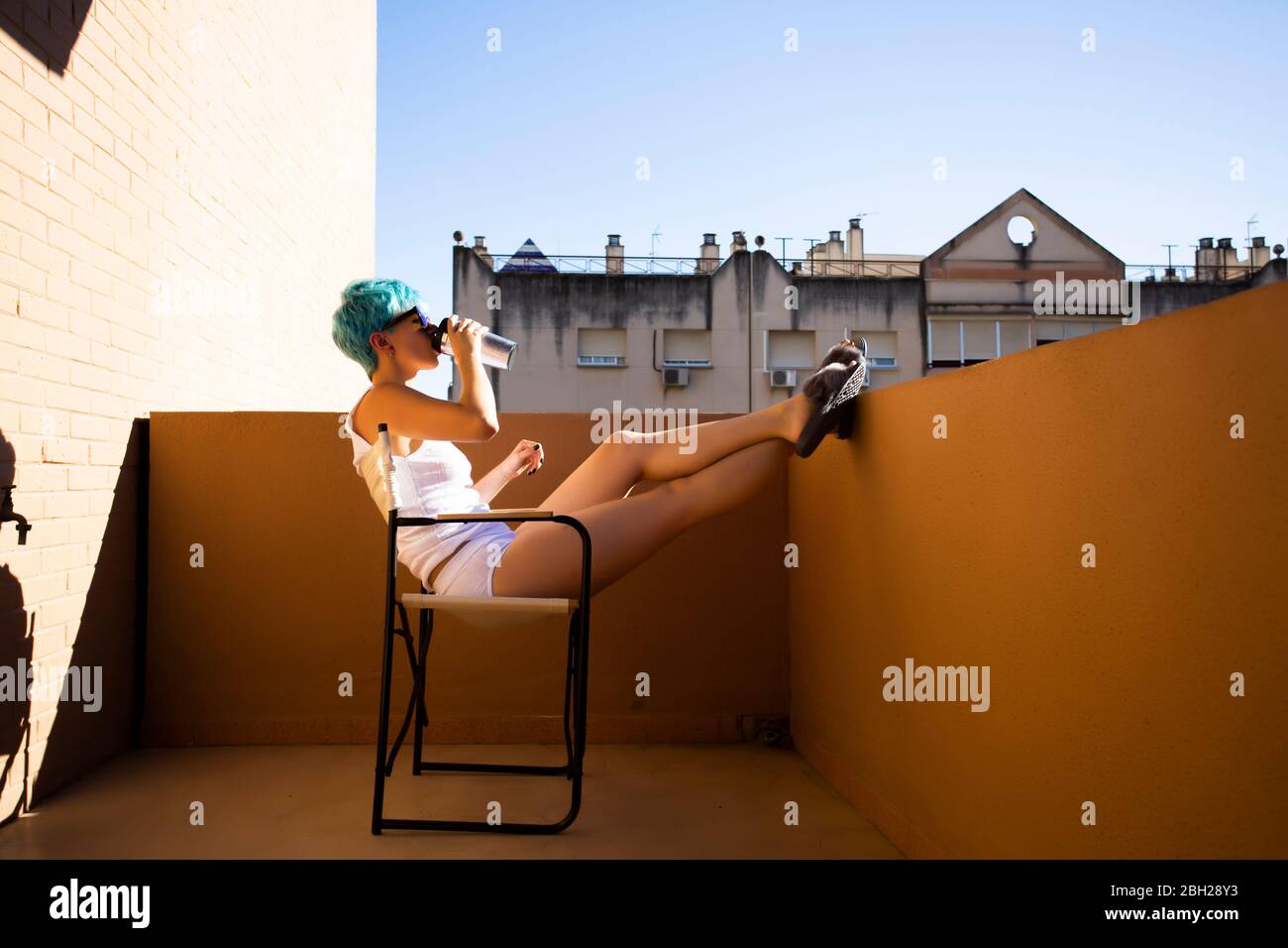 Androgyne young woman with blue hair drinking on the balcony Stock Photo