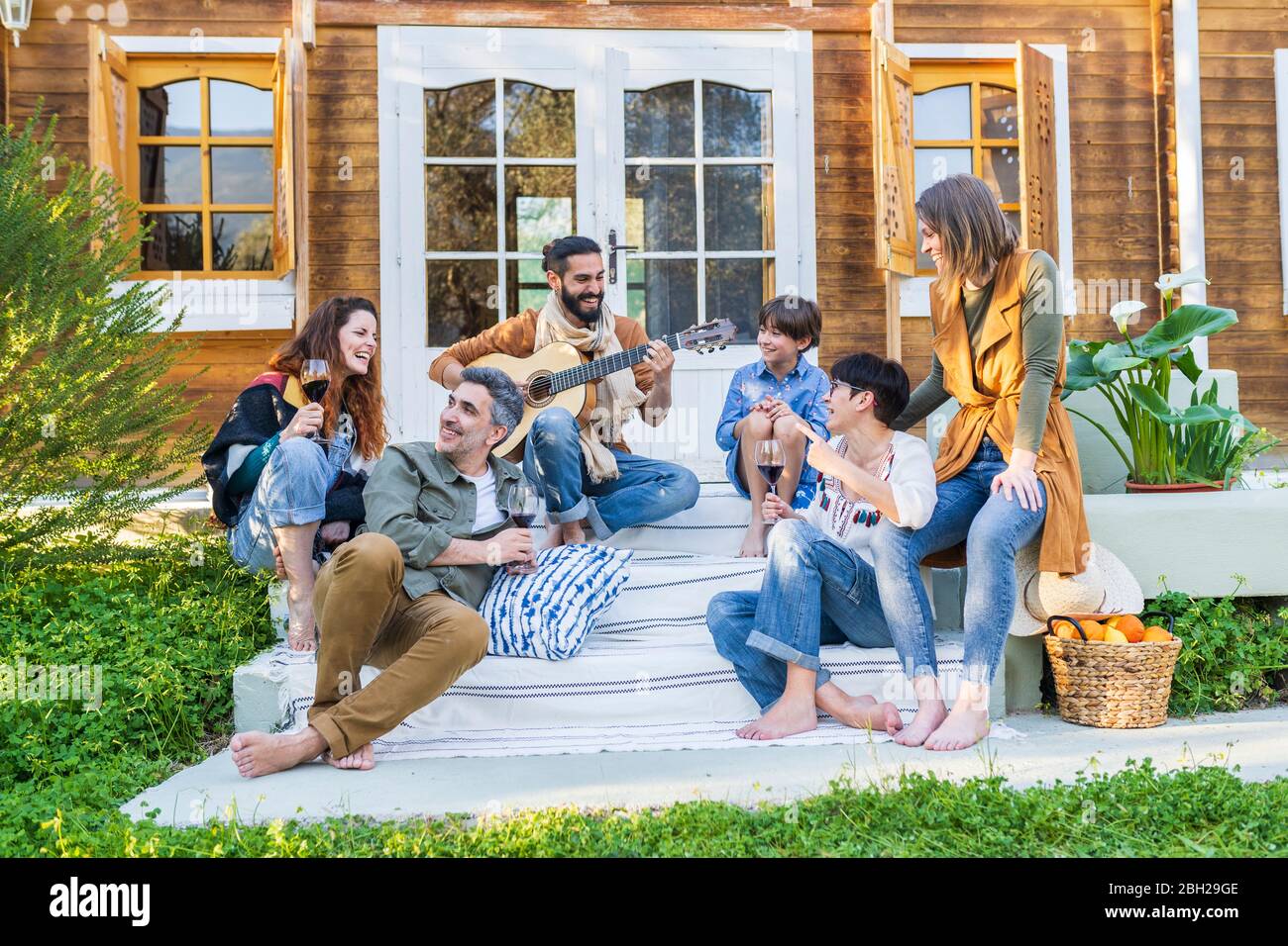 Friends playing music on the guitar and drinking wine outside a cabin in the countryside Stock Photo