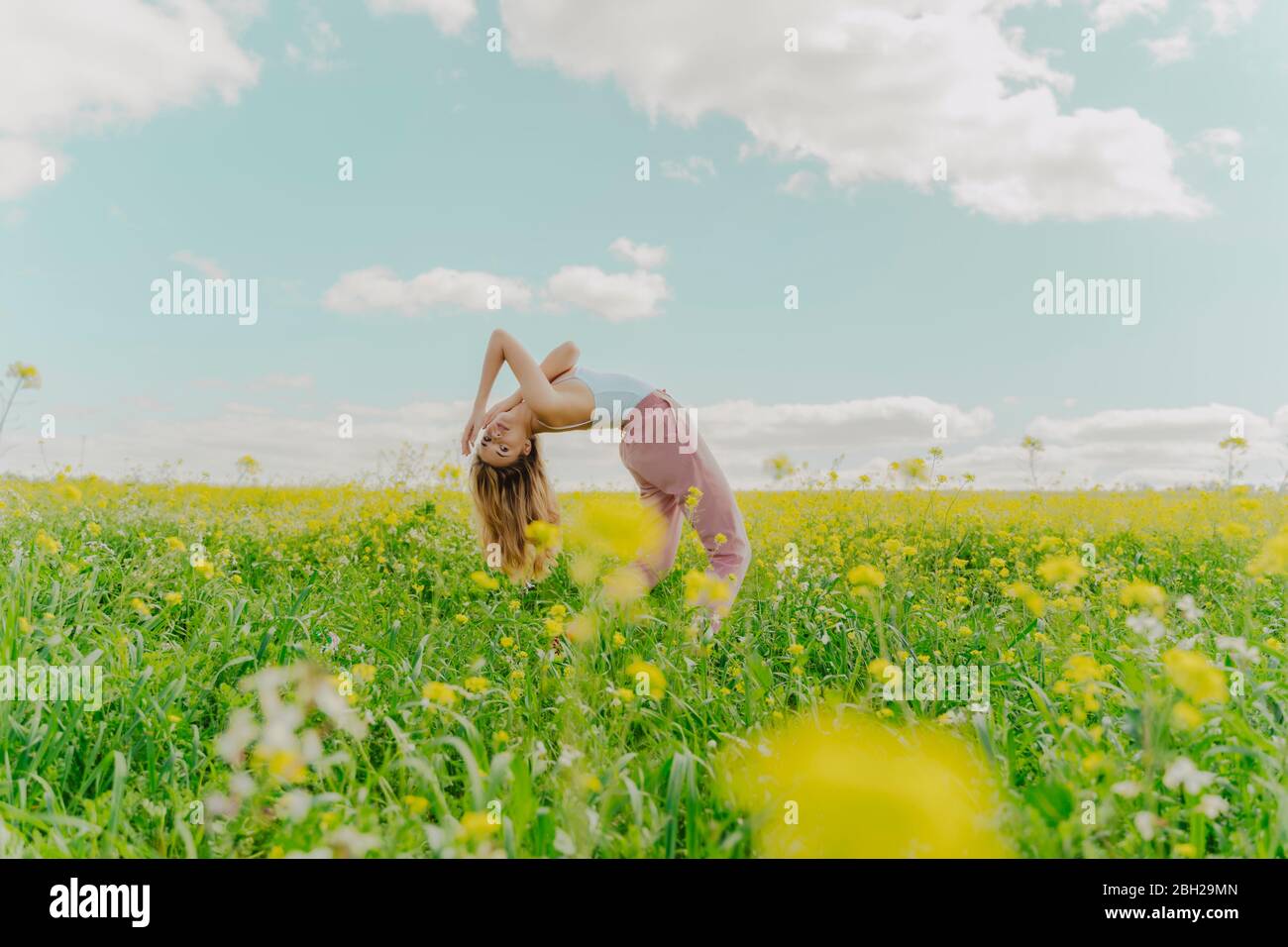 Young woman bending over backwards in a flower meadow in spring Stock