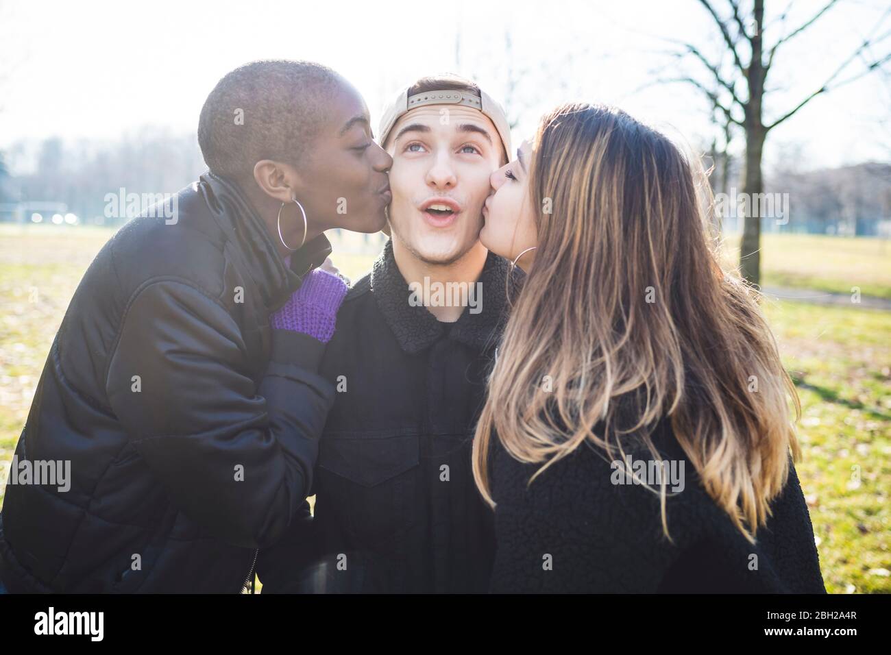 Two girls kissing their friend on his cheaks Stock Photo
