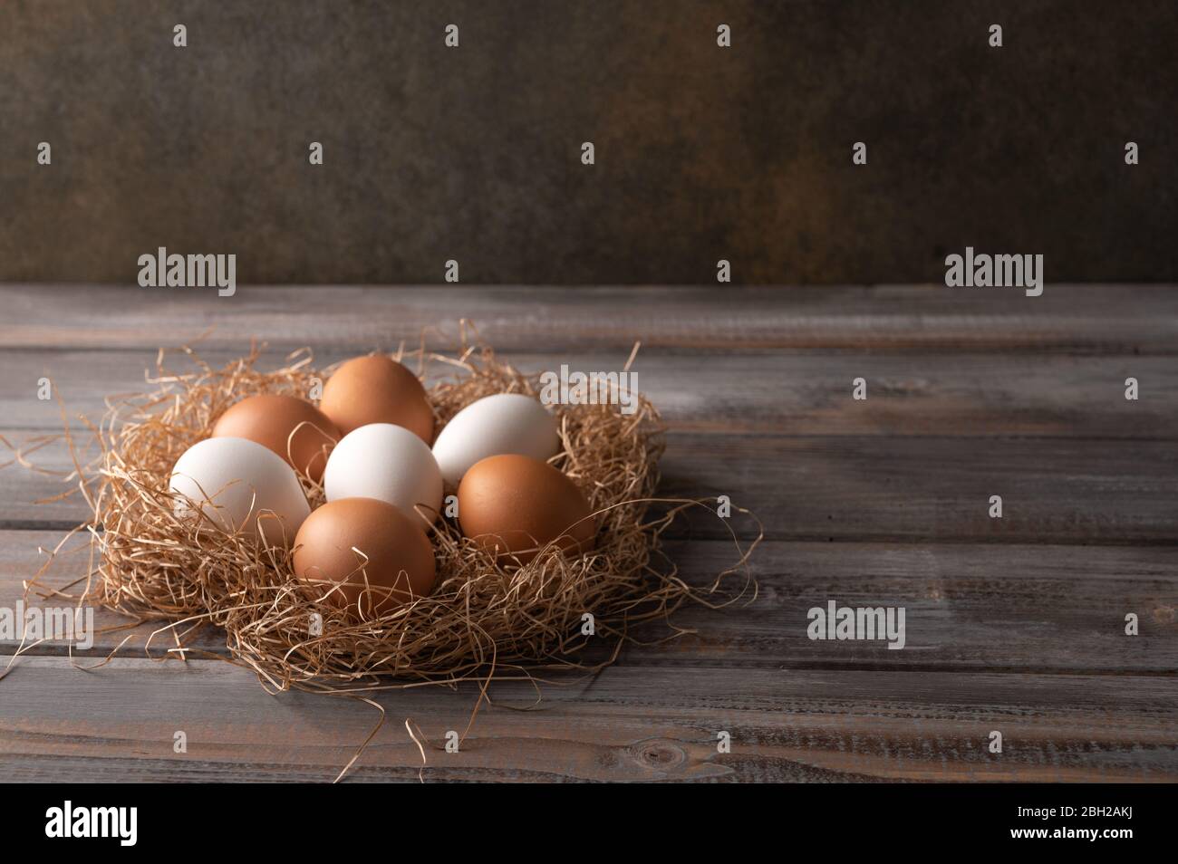 Brown and white chicken eggs in a straw nest on wooden background ...