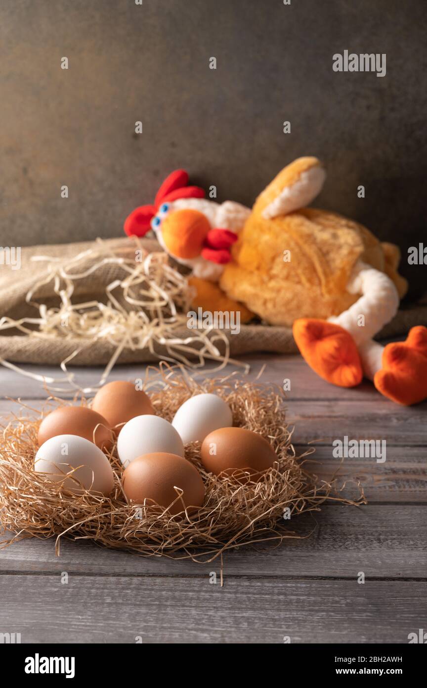 Brown and white chicken eggs in a straw nest on wooden background. Next ...