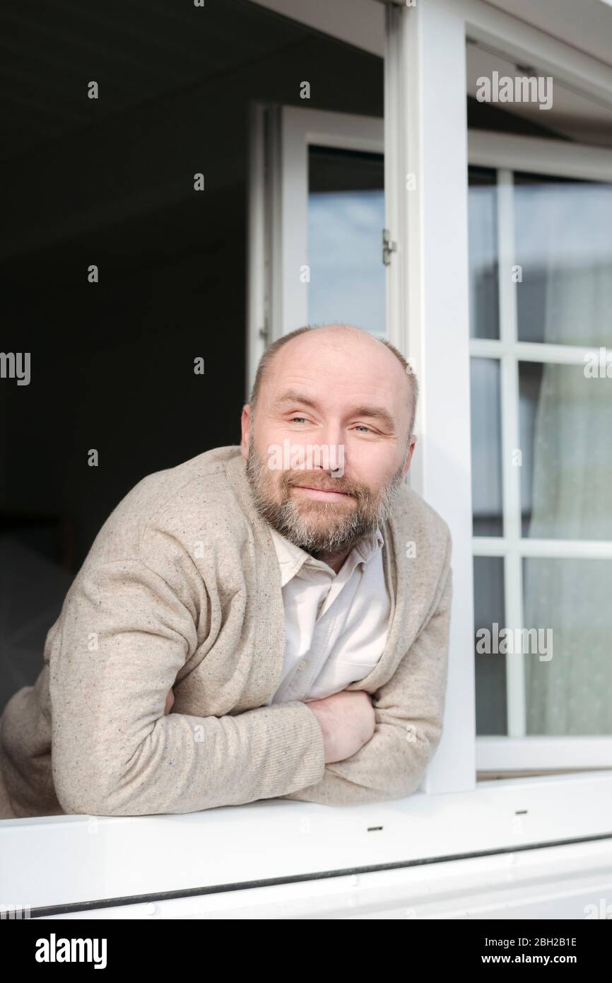 Portrait of relaxed mature man leaning out of window Stock Photo