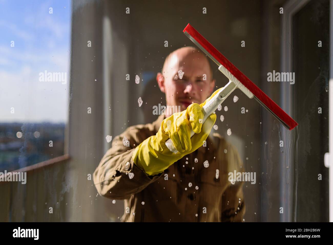 Man washing window in yellow rubber gloves with spray cleaner and ...