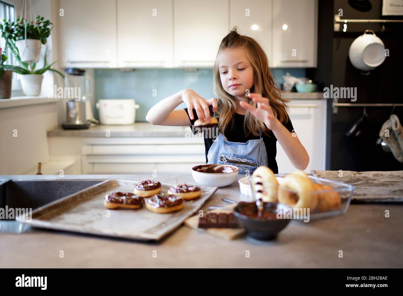 Portrait of smiling girl dipping home-baked doughnut into chocolate icing Stock Photo