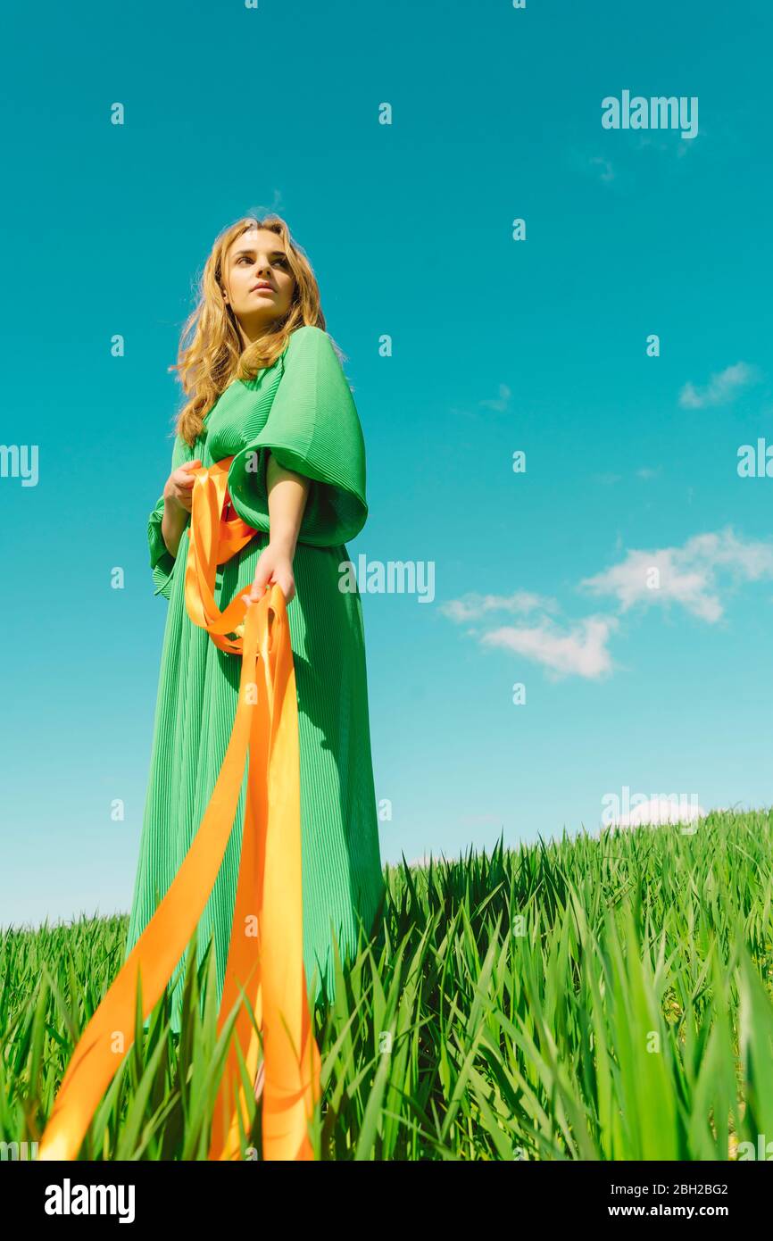 Young woman wearing a green dress standing in a field with ribbons ...