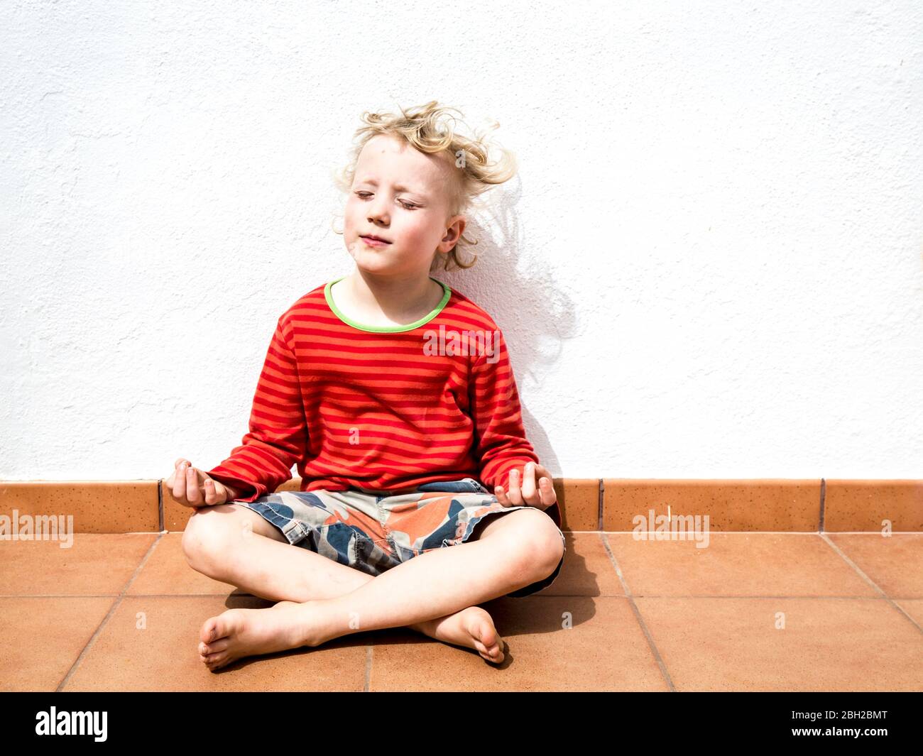 Portrait of blond little boy sitting in lotus position Stock Photo