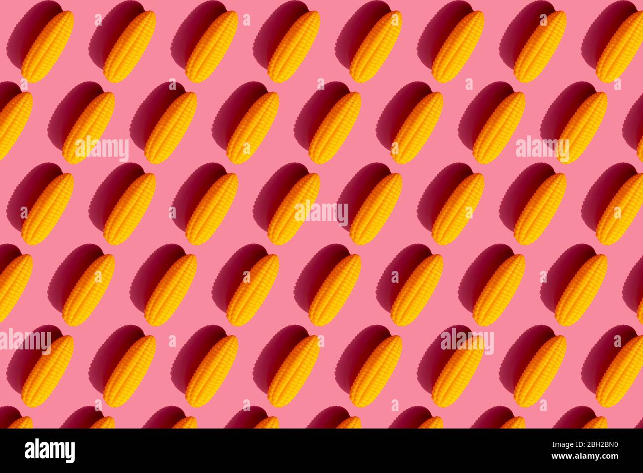 Pattern of yellow plastic corn cobs against pink background Stock Photo