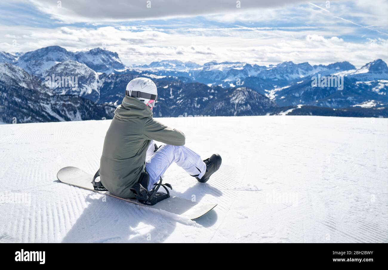Smiling woman sitting with snowboard on viewpoint and enjoying view at distance Stock Photo