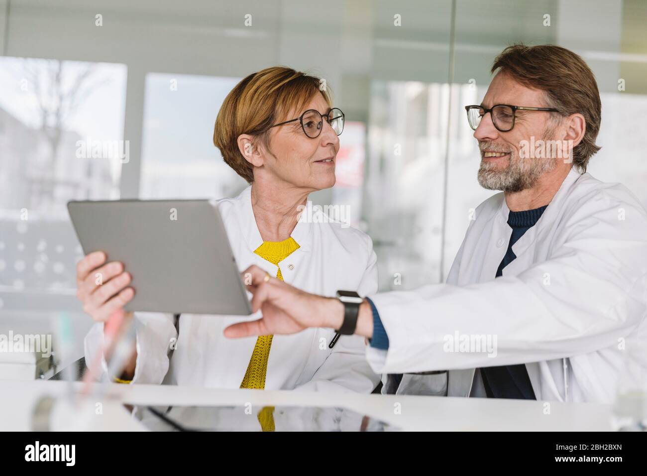 Two doctors sitting at desk using tablet Stock Photo