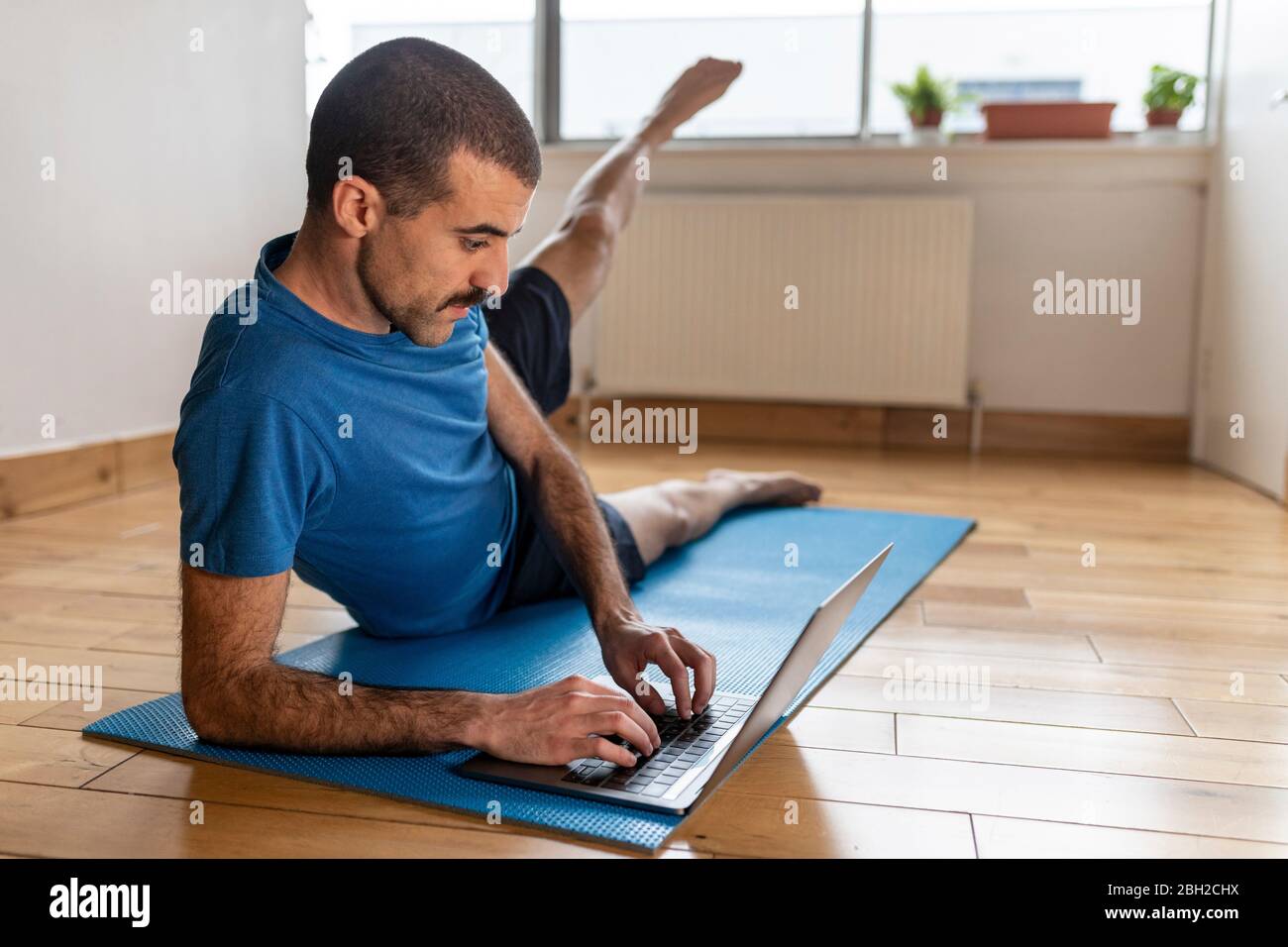 Sportive man lifting his leg and using laptop at home Stock Photo