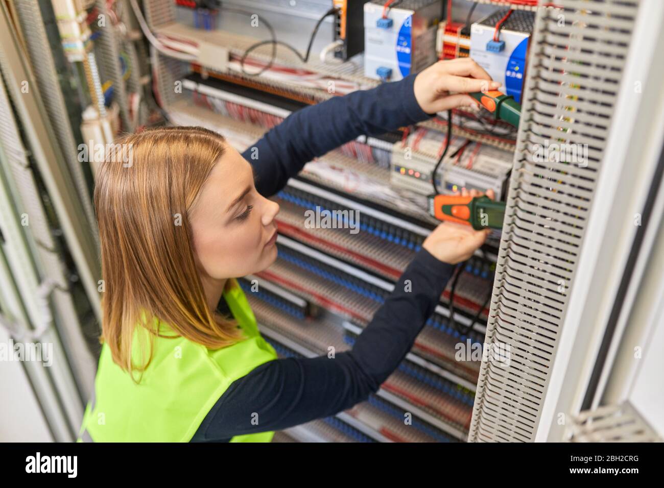 Female electrician working with voltmeter at fuse box Stock Photo