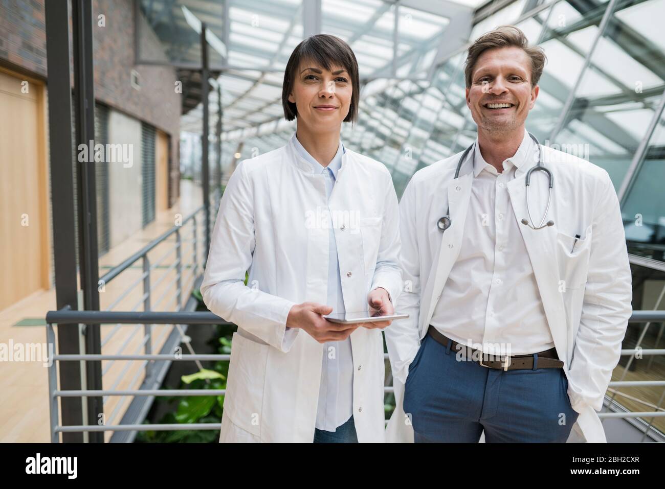 Two doctors standing in atrium, holding digital tablet Stock Photo
