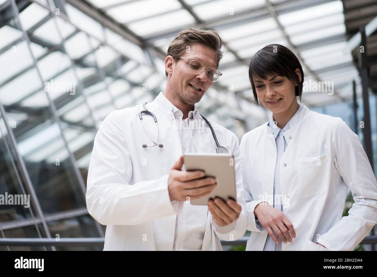 Doctor's standing in atrium, using digital tablet, discussing solutions Stock Photo