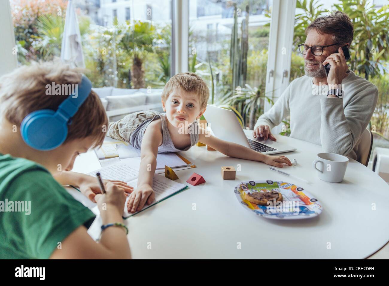 Father talking on the phone while sons are playing on the table Stock Photo
