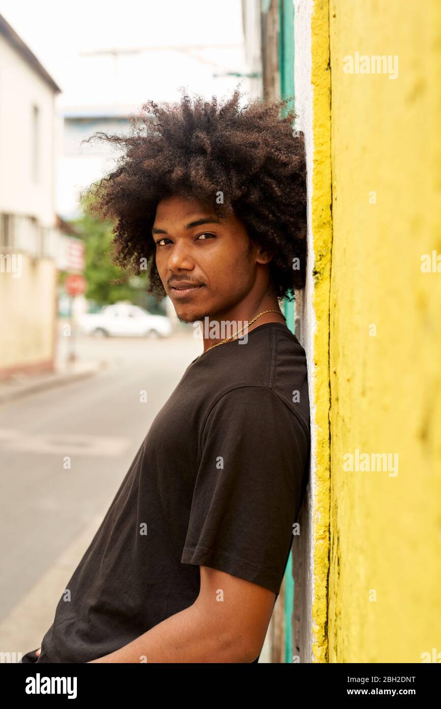 Portrait of young man with afro leaning against wall Stock Photo - Alamy