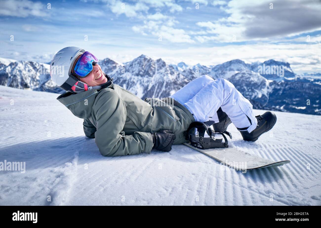 Smiling woman sitting with snowboard on viewpoint and looking at camera Stock Photo