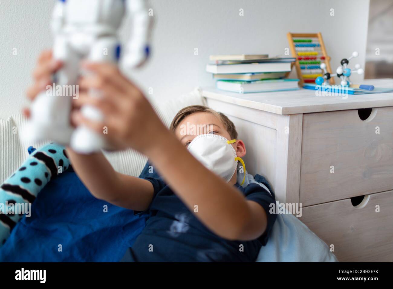 Boy with mask playing in his room during the corona crisis with his new, only friend, a robot Stock Photo