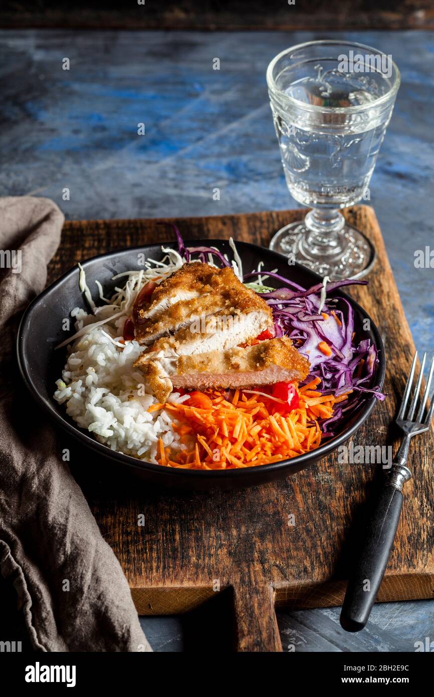Bowl of ready-to-eat salad with white and red cabbage, carrots, rice and chicken schnitzel Stock Photo