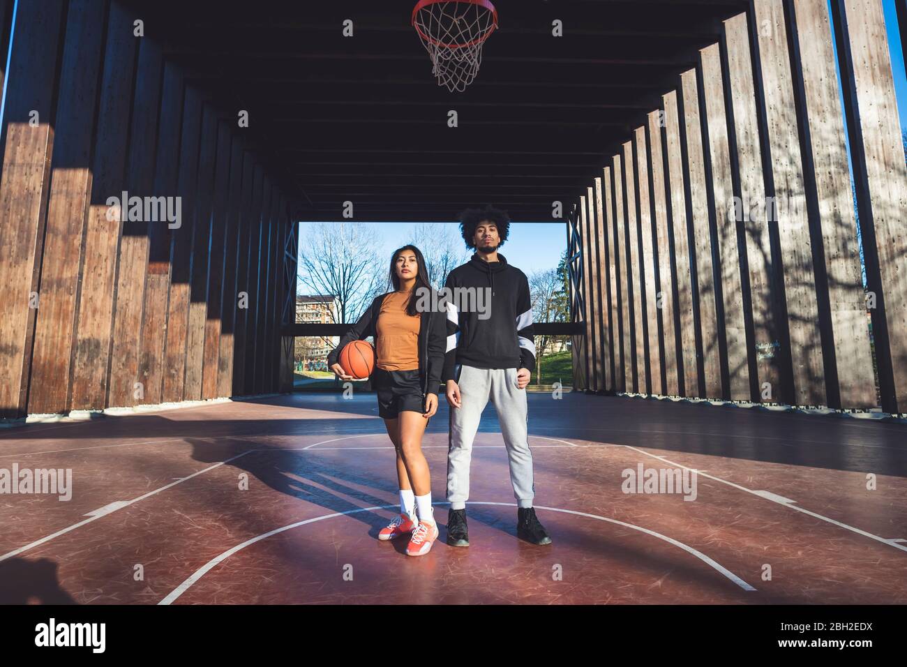 Portrait of young man and woman standing on basketball court Stock Photo