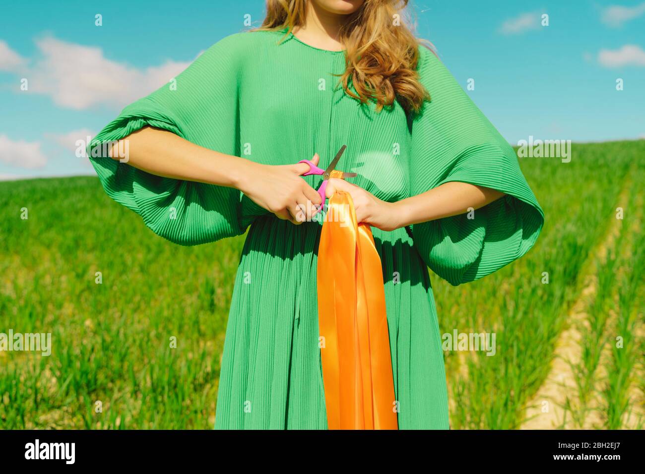 Mid section of woman wearing a green dress standing in a field cutting a ribbon Stock Photo