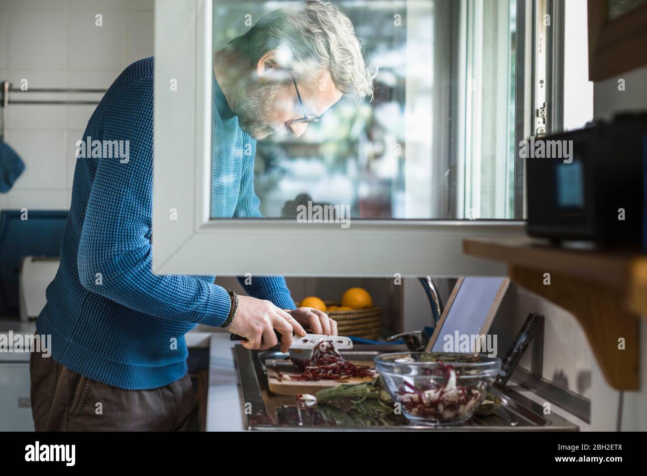 Mature man preparing salad at open window in his kitchen Stock Photo