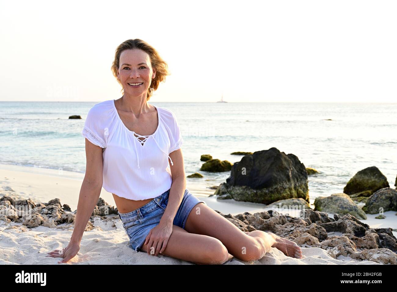 Woman sitting on the beach, looking at camera Stock Photo - Alamy