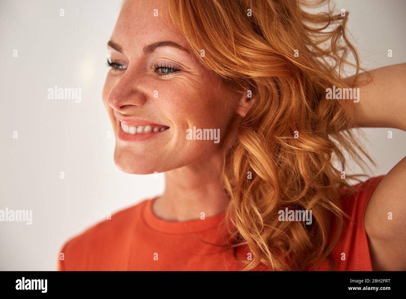 Portrait of red-haired woman, hand in hair, looking sideways Stock Photo