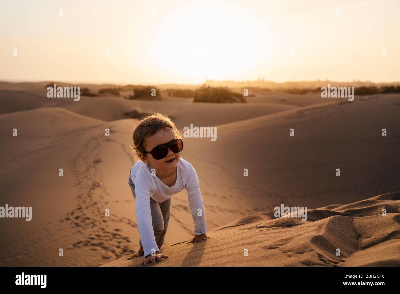 Girl crawling up sand dune, Gran Canaria, Spain Stock Photo