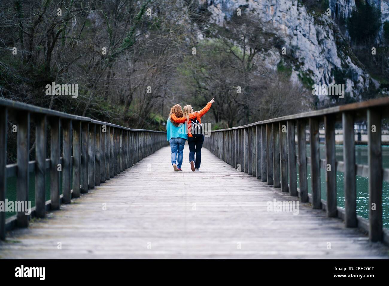 Back view of two best friends walking side by side on boardwalk