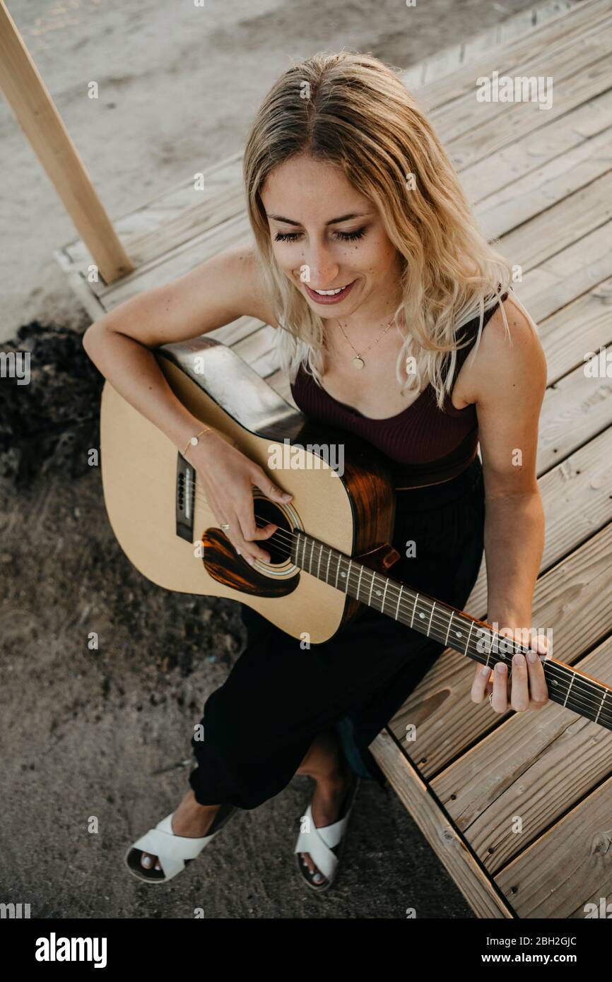 Smiling blond woman playing guitar outdoors, California, USA Stock Photo