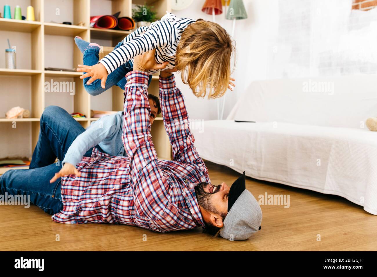 Father lying on floor, holding daughter aloft, pretending to fly Stock Photo