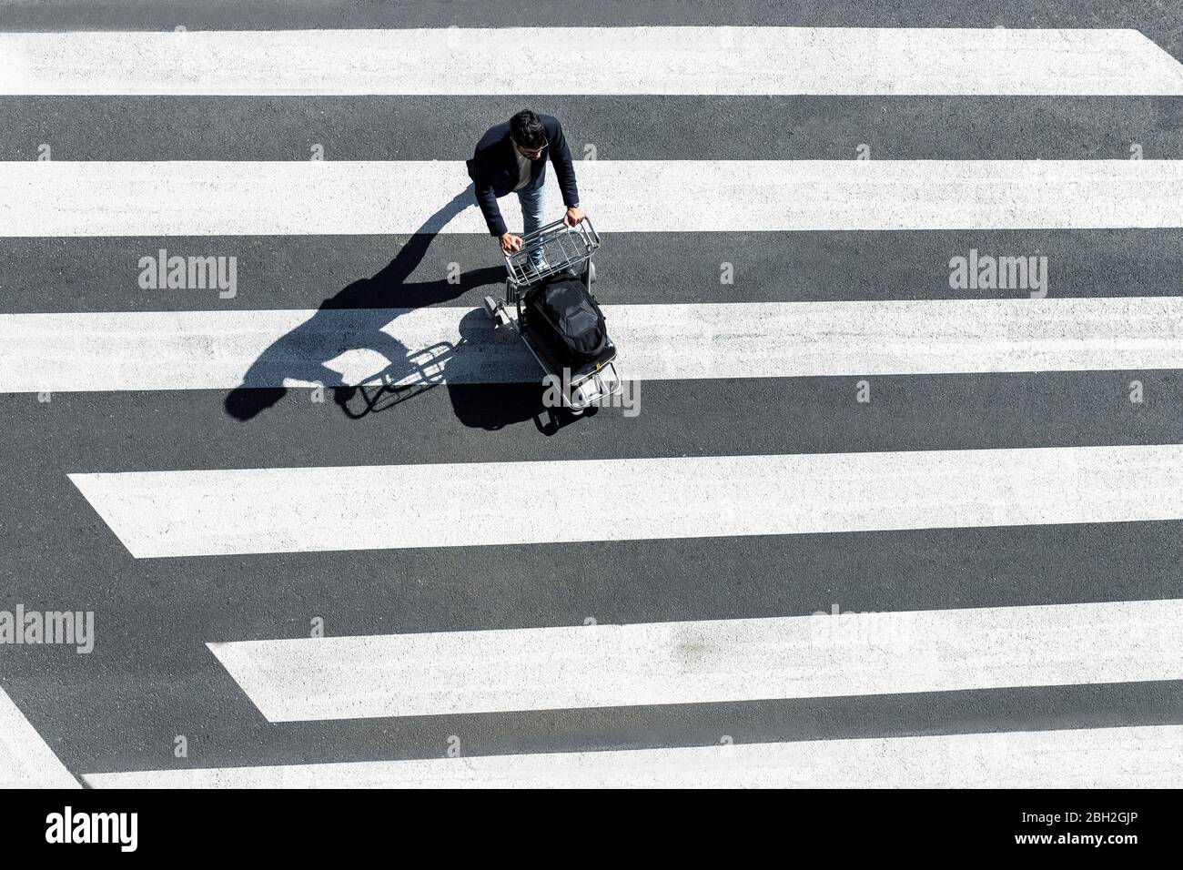 Man on zebra crossing pushing baggage cart, top view Stock Photo