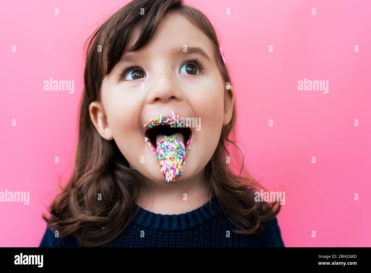Portrait of happy little girl with sugar granules on lips and tongue in front of  pink background Stock Photo