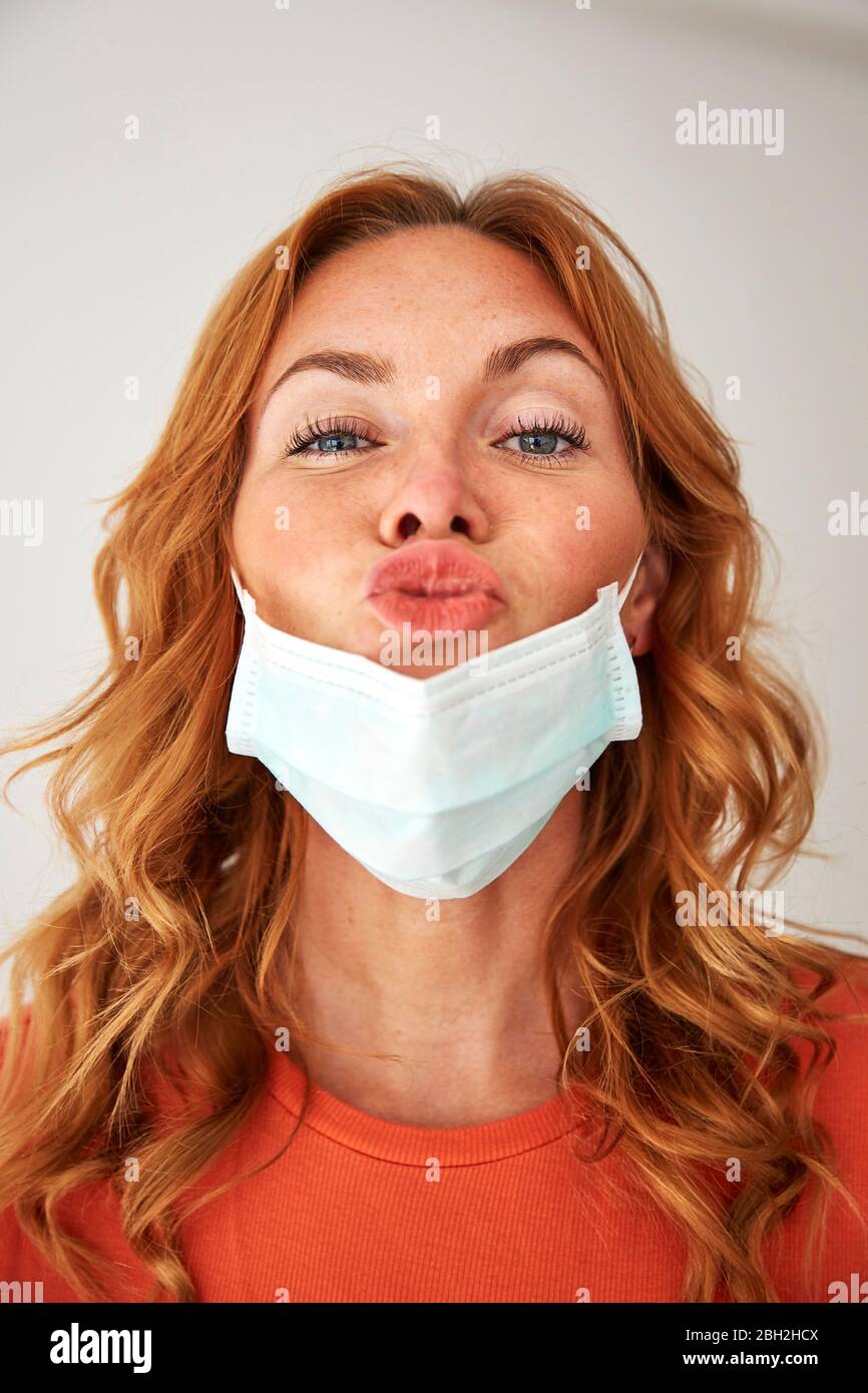 Portrait of red-haired woman with kissing lips over a protective mask Stock Photo