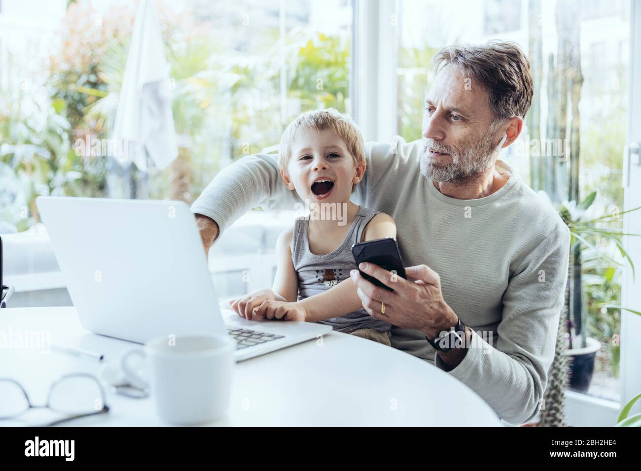 Little boy sitting on lap of father, traying to work from home Stock Photo