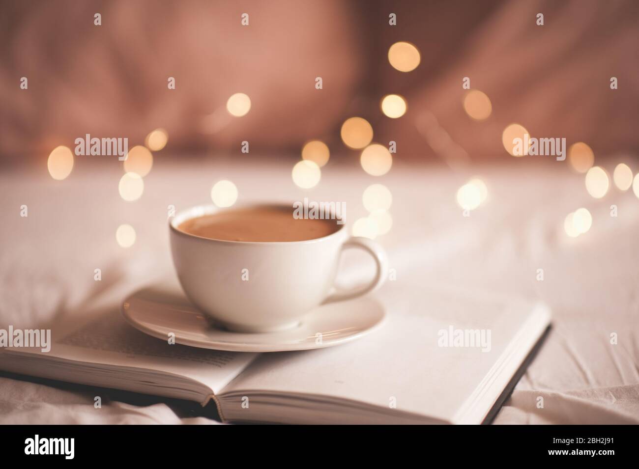 Fresh cup of coffee on paper book over glowing lights closeup ...