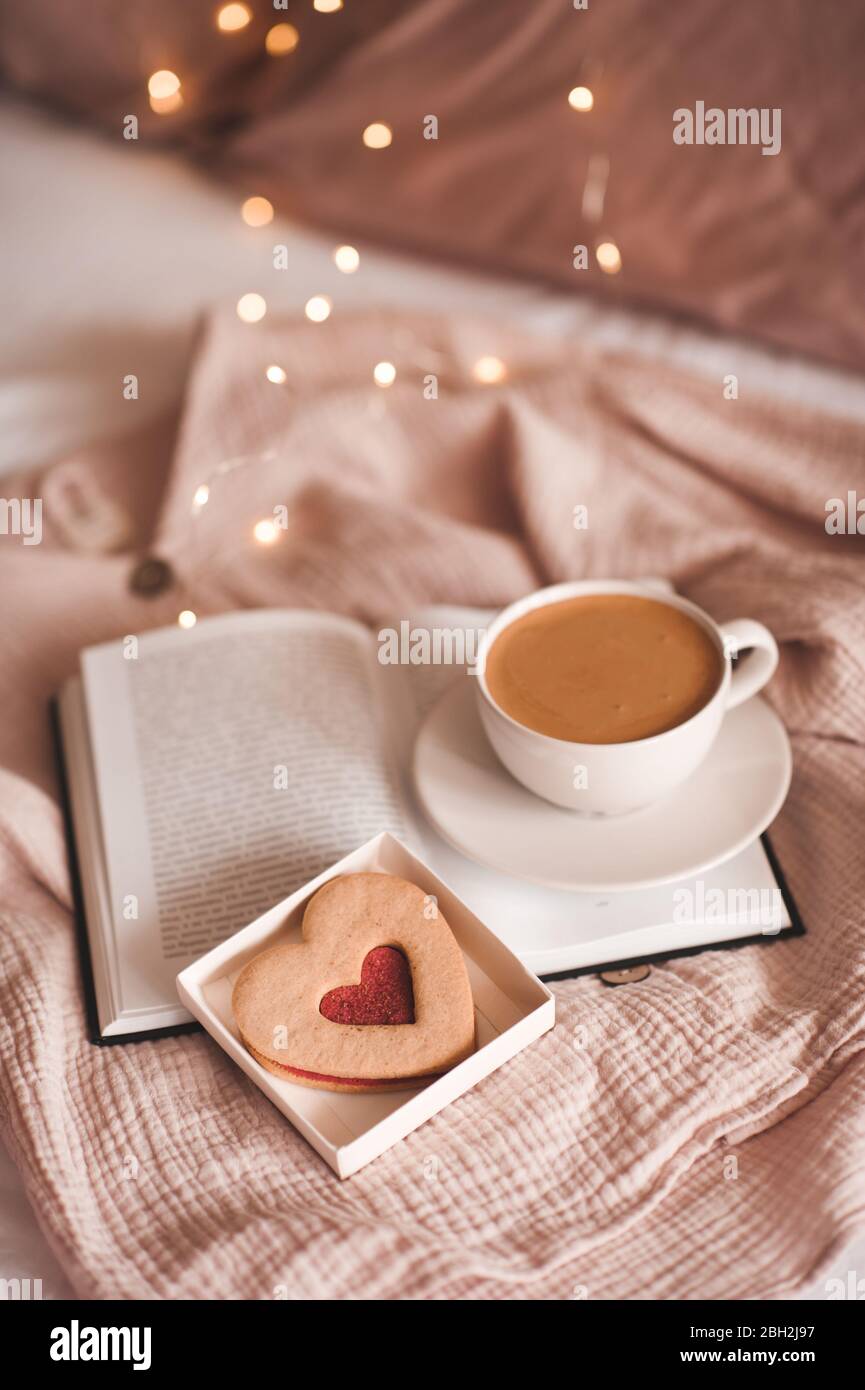 Cup of coffee with heart shape cake in bed closeup. Good morning ...